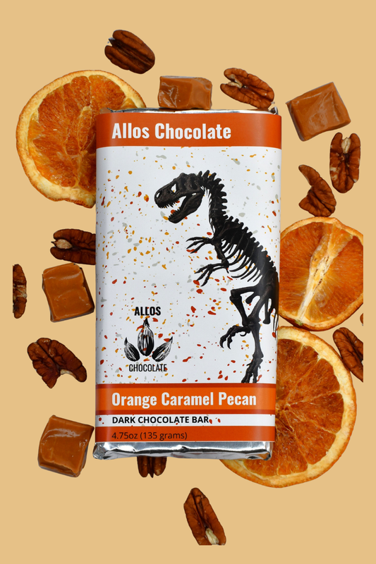 Allos Chocolate Orange Caramel Pecan dark chocolate bar with decorative packaging on a beige background with chocolate pieces and oranges.
