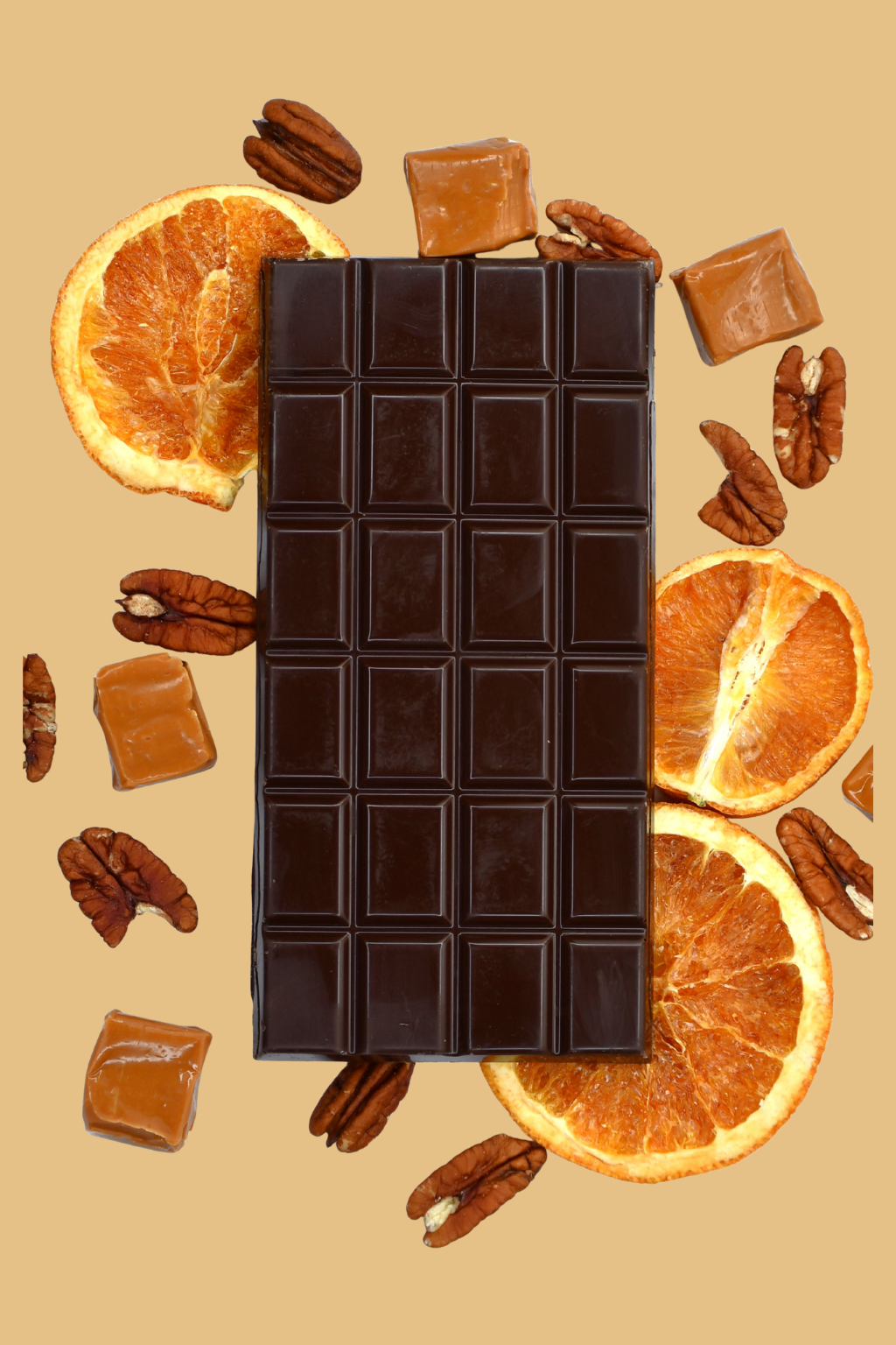 Dark chocolate bar surrounded by dried oranges, pecans, and caramel pieces on a beige background